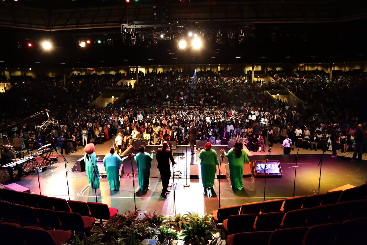 Farmedia live gospel concert — packed arena with thousands of attendees and performers on stage under dramatic stage lighting